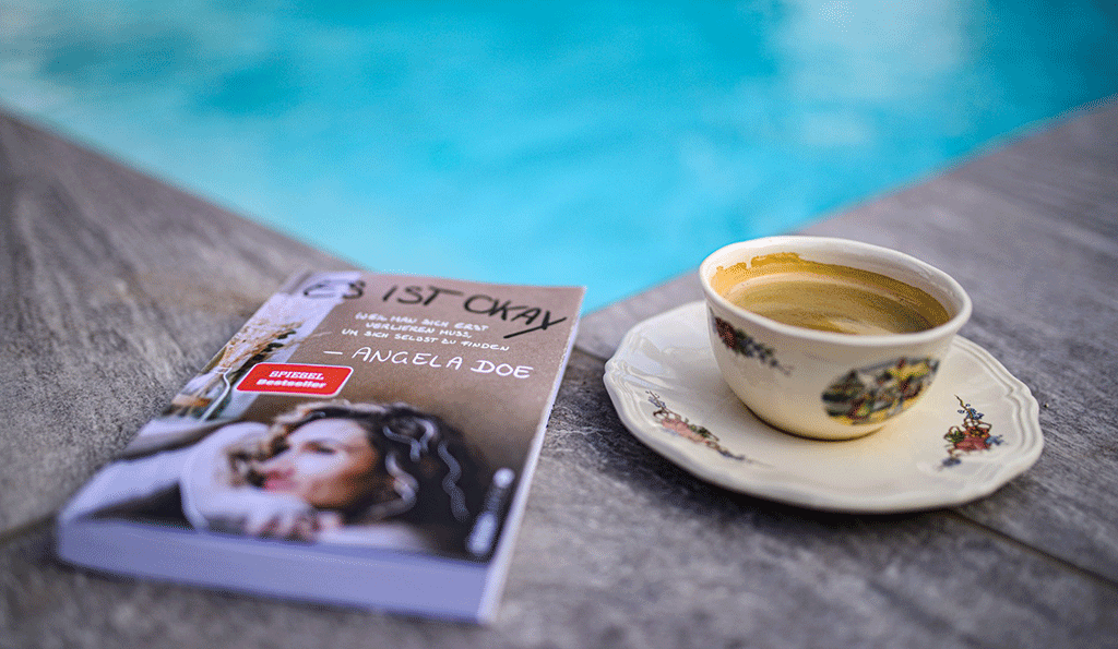 Buch "Es ist okay" mit Kaffee am Pool