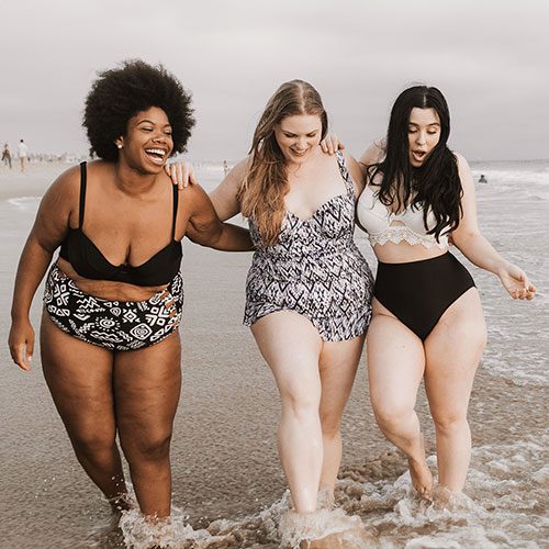 Drei Frauen mit unterschiedlichen Körpertypen lachen am Strand