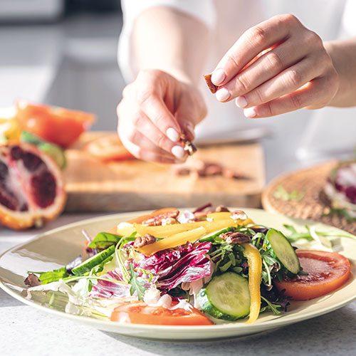 Ein Teller mit Salat, zu dem jemand noch Nüsse hinzugibt
